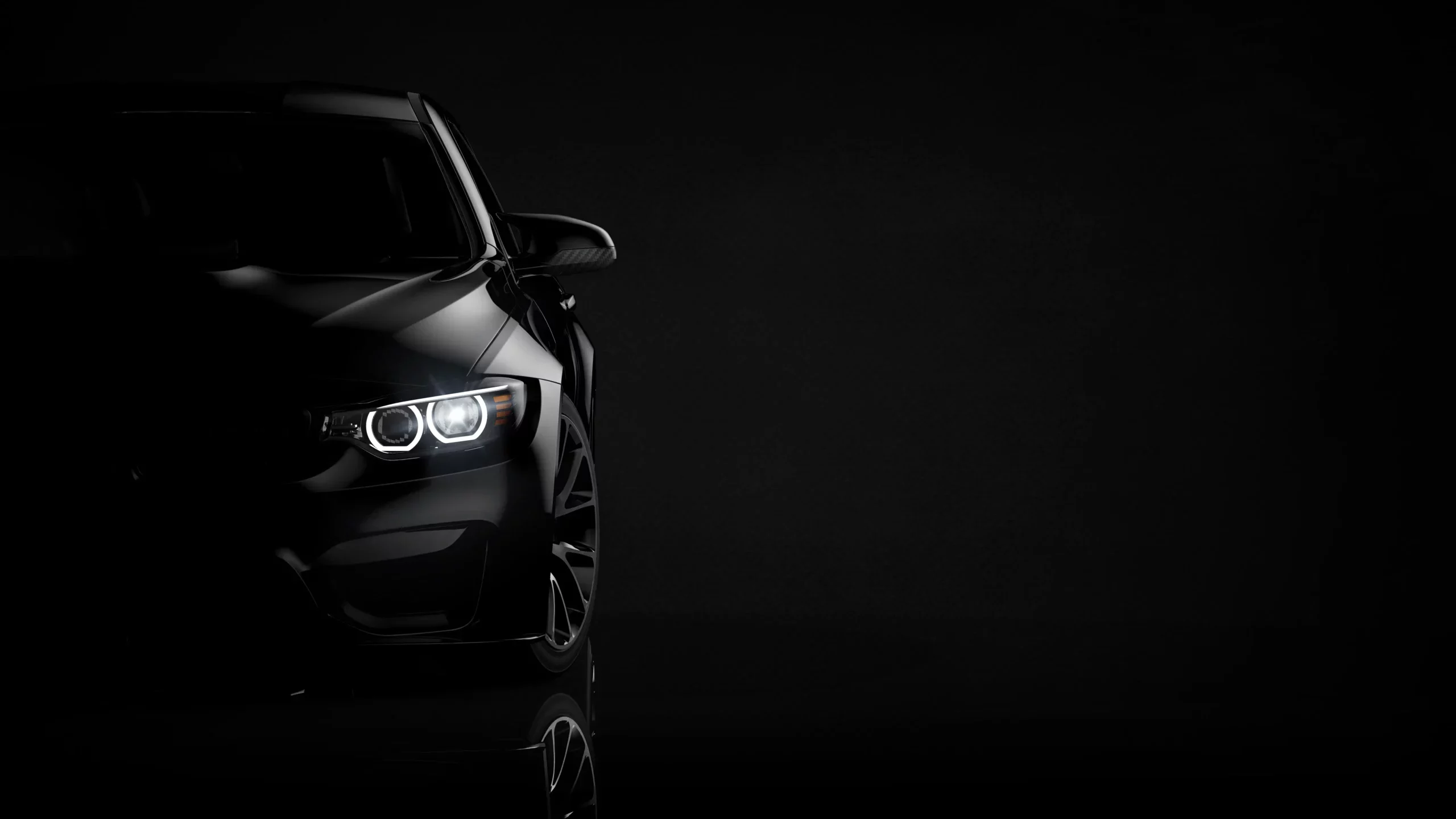 Front of a dark luxury car at night with headlights on