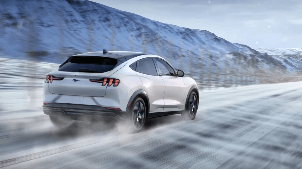 Rear view of a white electric SUV driving on a snowy road surrounded by a mountainous winter landscape