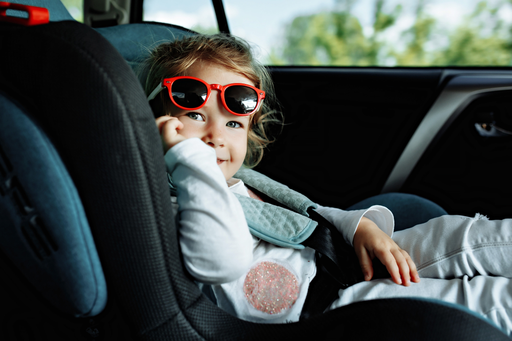 infant in car seat smiling with red sunglasses on